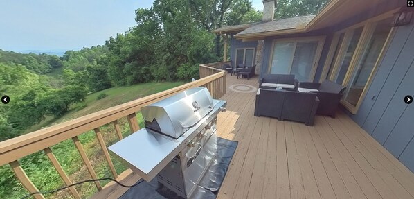 A deck with a grill, outdoor furniture, and a scenic view of the forest.