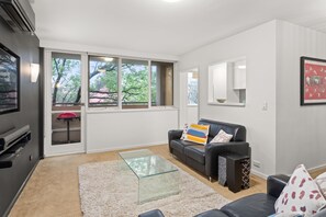 A modern living room with a glass coffee table, a black leather sofa, and a large window with a view of trees. - Mama Koko Pet Friendly Retreat in Hawthorn East (Hawthorn East)