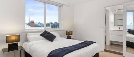 A modern bedroom with a large bed, bedside lamps, a window, and a mirror.