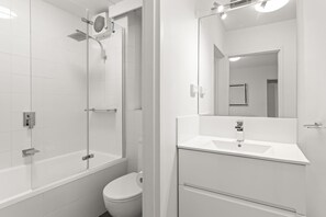 Un baño moderno con cabina de ducha de vidrio, inodoro blanco y tocador con espejo.