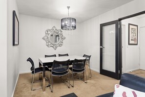 A dining area with a white table, black chairs, a chandelier, and a mirror on the wall.