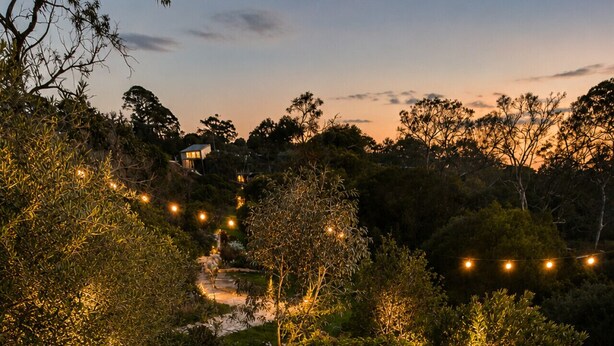 An outdoor seating area with round tables and chairs, surrounded by trees and a string of lights.