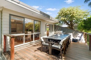 A modern house with a deck, a dining area with a table and chairs, and a barbecue grill. - Peaceful waves – Short walk to the Beach (Rye)