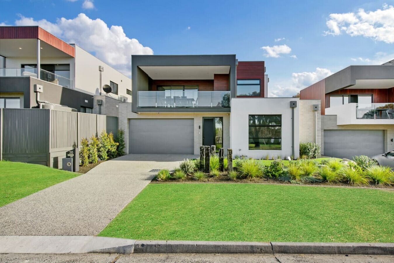 A modern two-story house with a flat roof, large windows, and a well-maintained lawn.