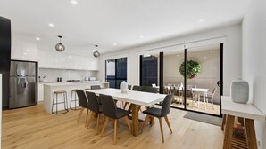Una cocina moderna con armarios blancos, un refrigerador de acero inoxidable y un comedor con mesa y sillas blancas.