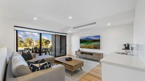 Una sala de estar moderna con sofá, mesa de centro y televisor. Hay un ventanal corredizo que da a un espacio exterior.