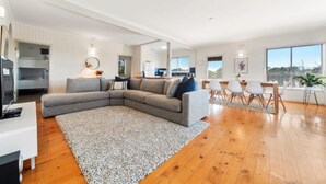A modern living room with a sectional sofa, a dining area with a wooden table and chairs, and a kitchen in the background.