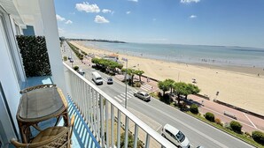 Un balcón con sillas de mimbre con vista a una playa y una carretera con coches.
