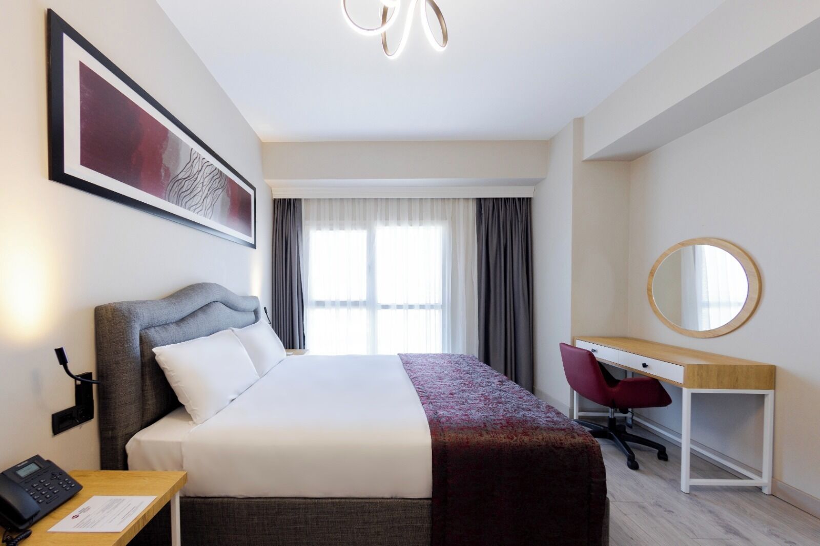 A hotel room with a bed, desk, chair, and a large window with curtains.