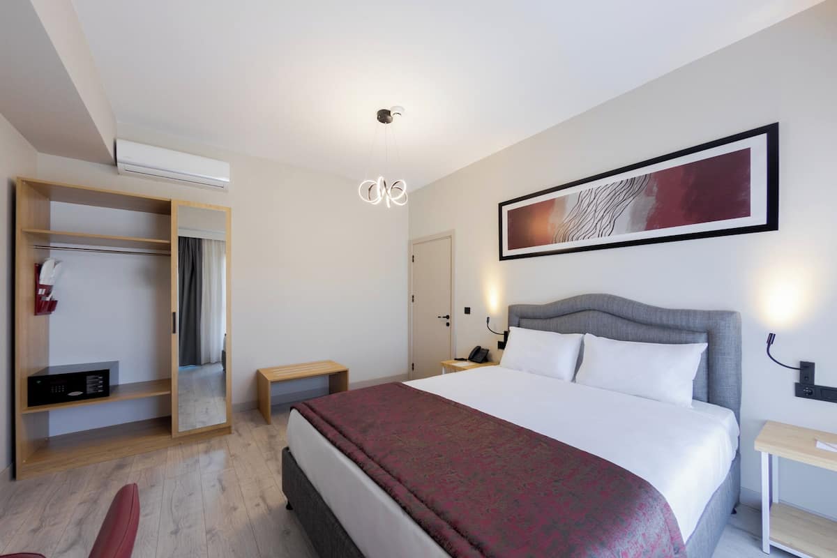 Ein Hotelzimmer mit einem großen Bett, einem Kleiderschrank, einem Nachttisch und einem an der Wand hängenden Kunstwerk.