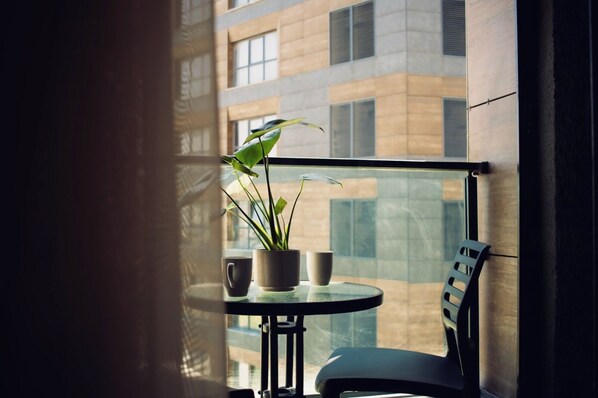 Un balcón con una mesa, dos tazas, una planta en maceta y una silla.