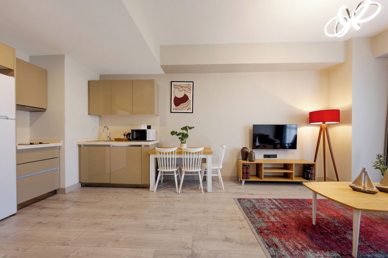 Eine moderne Küche mit integrierten Geräten, ein Essbereich mit Tisch und Stühlen, ein Fernseher und eine rote Stehlampe.