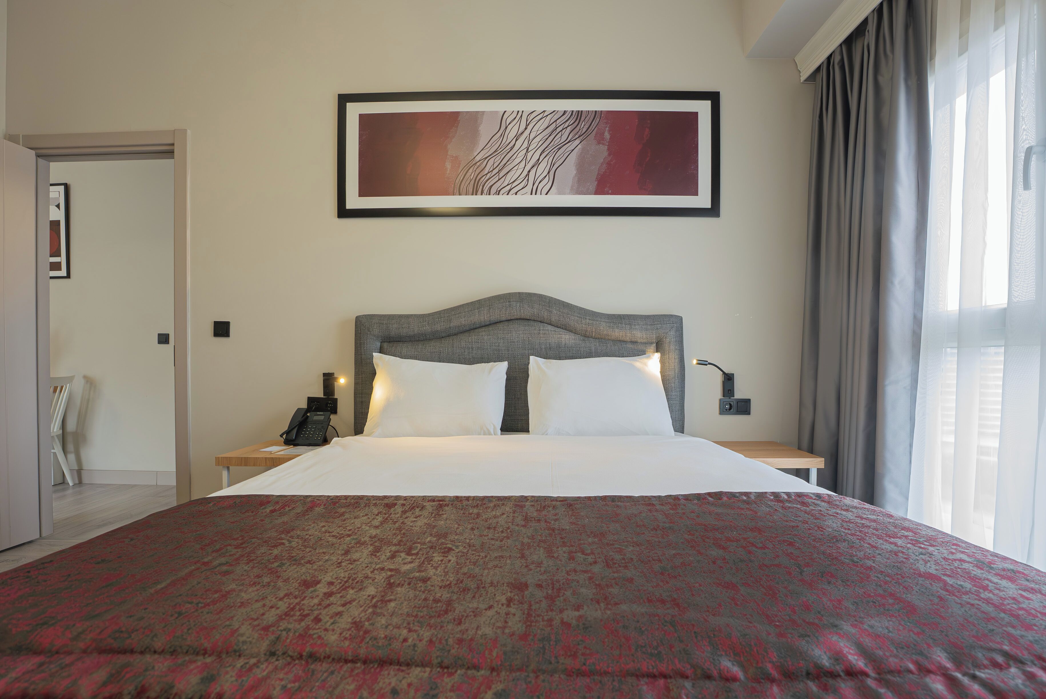 Een net opgemaakt bed met een bedsprei met een patroon, een lijst met een abstract schilderij erboven en een nachtkastje met een lamp.