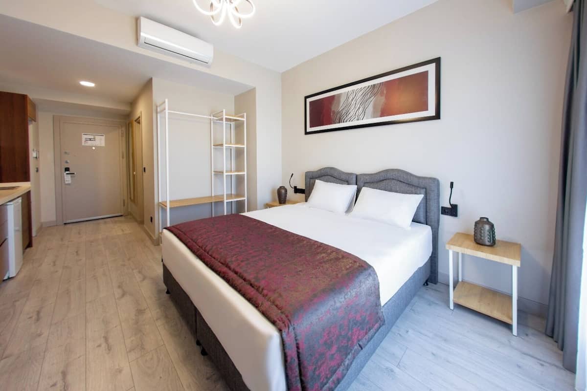 Ein Hotelzimmer mit Bett, Nachttischen, einem Kleiderschrank, einer Klimaanlage und einem gerahmten Kunstwerk an der Wand.