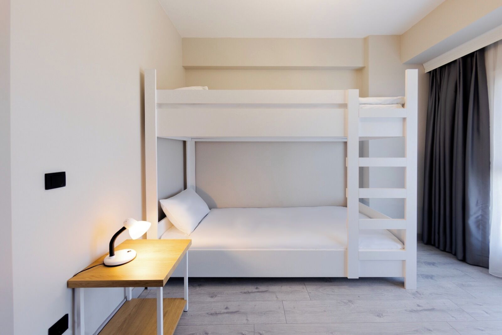 Camera con letto a castello, una scrivania, una lampada, una scala e una finestra con tende.