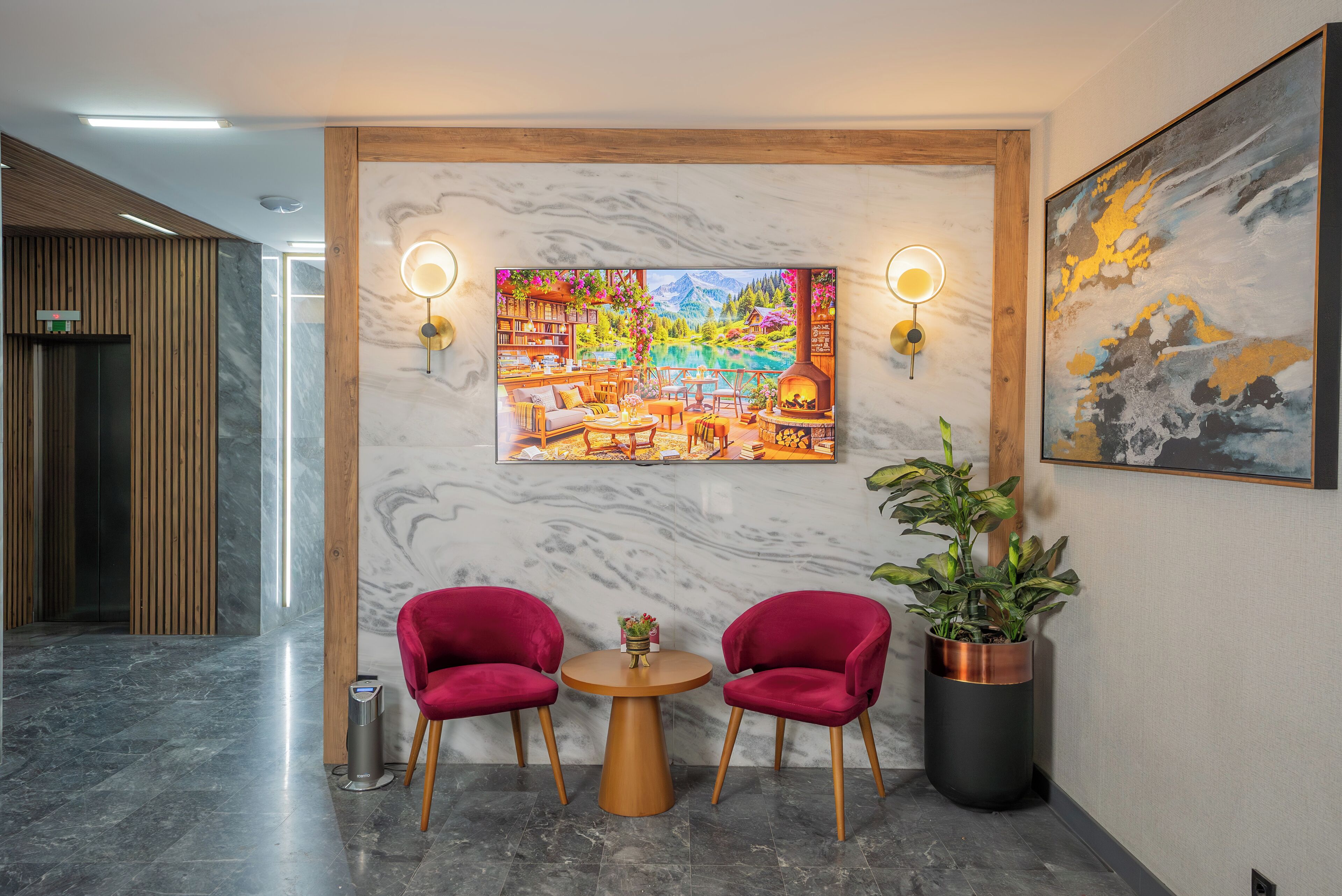 A lobby with a marble wall, two red chairs, a round table, a potted plant, and a painting.