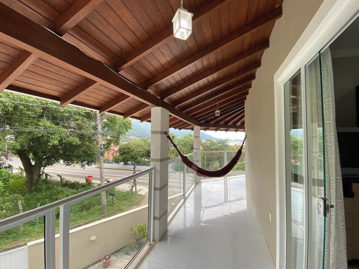 Un balcon doté d’un plafond en bois, de portes vitrées et offrant une vue sur la verdure et une route.