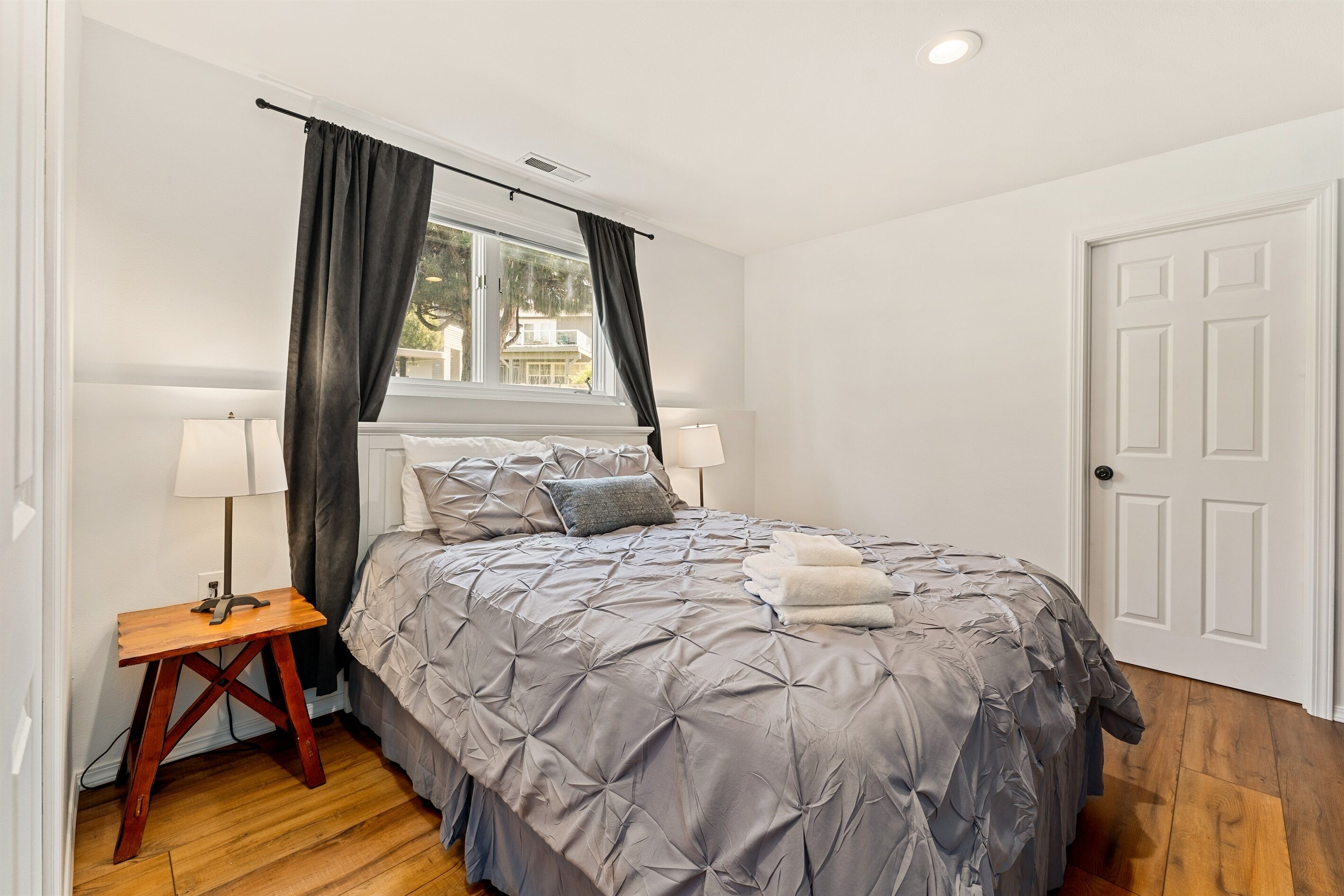 Un dormitorio con cama, dos mesitas de noche, una ventana con cortinas y una puerta.