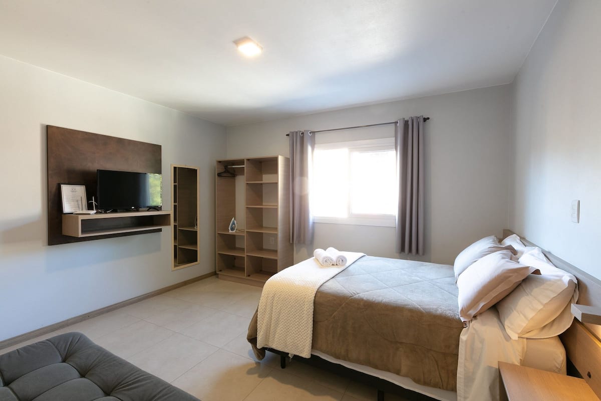 A bedroom with a bed, a TV mounted on the wall, a wardrobe, and a window with curtains.