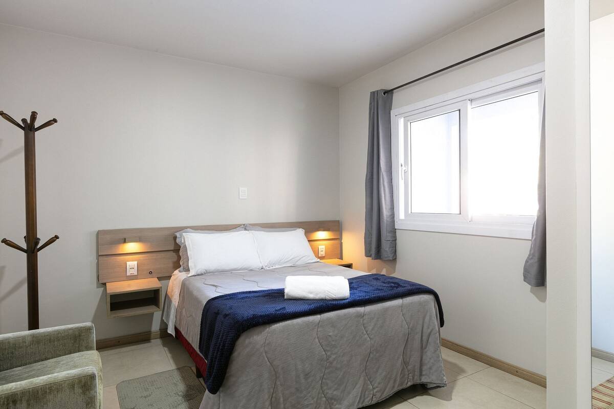 A bedroom with a bed, bedside tables, a coat rack, and a window.