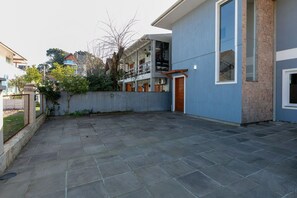 Un patio con piso de piedra, un edificio azul con balcón y una valla.