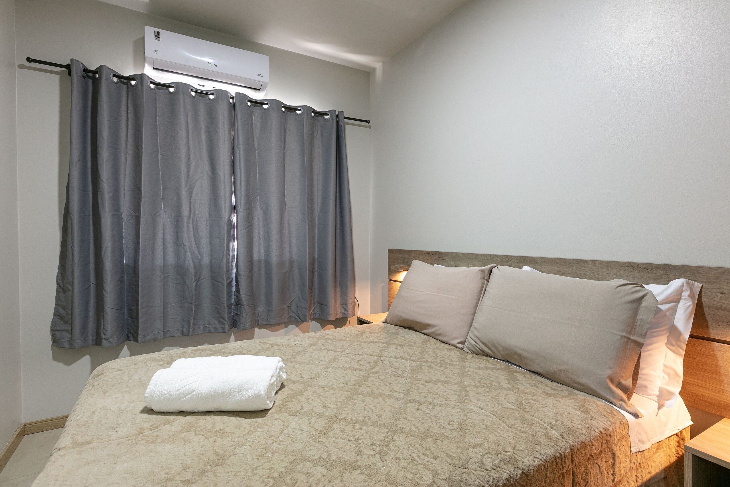 Hotelkamer met een bed, een raam met gordijnen, een airconditioning en een nachtkastje met een lamp.
