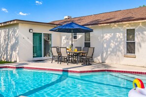A swimming pool with a table and chairs under a blue umbrella, a door, and a window. - Luxurious Spa Retreat with Stunning Pool in Palm Harbor (Palm Harbor)