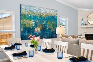 Un coin repas avec une table dressée pour quatre personnes, une grande peinture abstraite accrochée au mur et un canapé à l’arrière-plan.