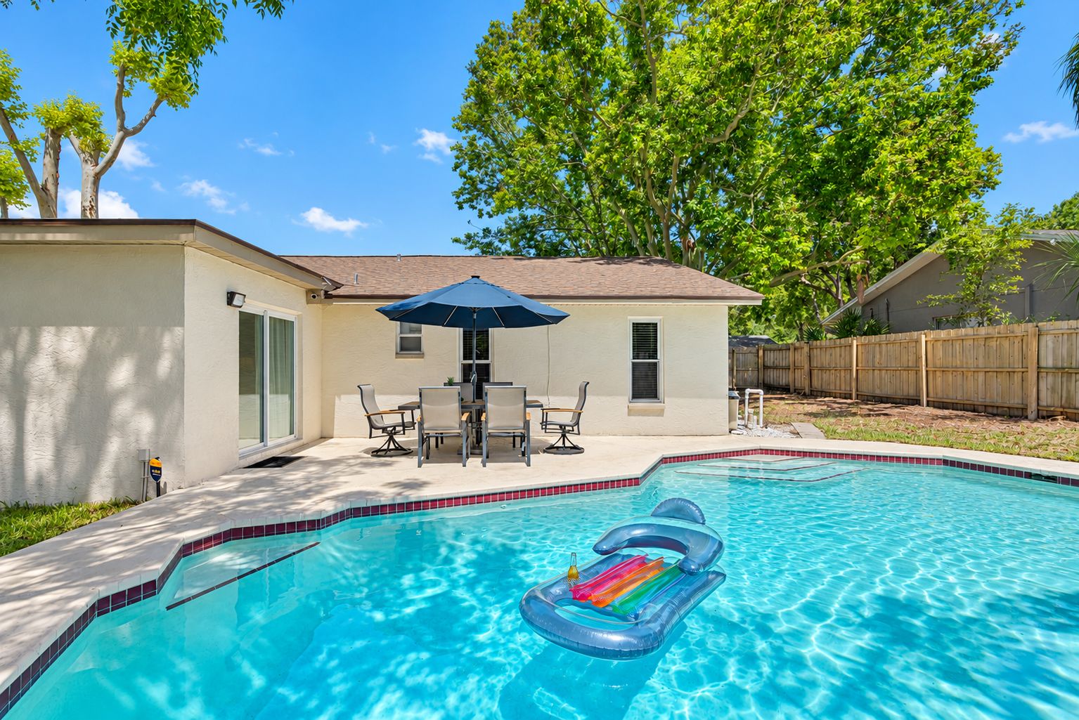 Un jardin avec une piscine, une table de patio entourée de chaises et une clôture en bois.