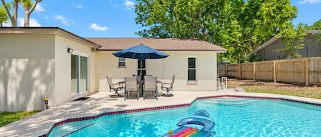 Un jardin avec une piscine, une table de patio entourée de chaises et une clôture en bois.