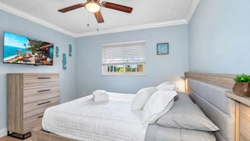 Une chambre à coucher comprenant un lit, un ventilateur de plafond, une commode, une fenêtre avec des stores et un téléviseur fixé au mur.