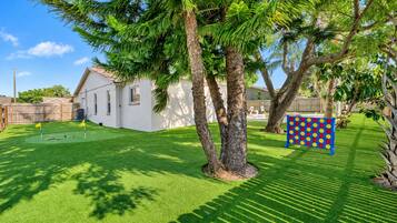A backyard with artificial grass, a swing set, and a play area with a colorful board game.