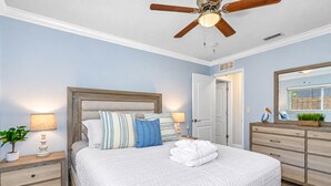 Une chambre à coucher comprenant un lit, des tables de chevet, une commode, un ventilateur de plafond et une porte.