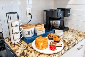 Eine Küchenarbeitsplatte mit Kaffeetassen, einer Kaffeemaschine, einer Muffin-Form und einem Teller mit Gebäck.