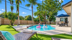 Un jardin avec une piscine, des chaises longues et un coin repas.