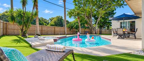 A backyard with a swimming pool, lounge chairs, and a dining area.
