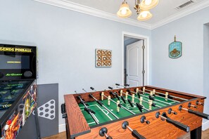Une table de baby-foot dans une pièce où se trouvent également un flipper et une porte donnant sur une autre pièce.