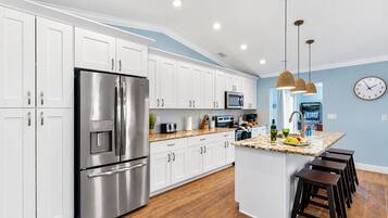 A modern kitchen with white cabinets, stainless steel appliances, a granite countertop, and a central island with stools.