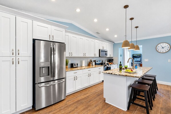 A modern kitchen with white cabinets, stainless steel appliances, a granite countertop, and a central island with stools.
