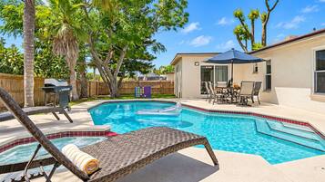A backyard with a swimming pool, a grill, and a covered patio area.