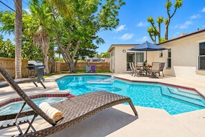 A backyard with a swimming pool, a grill, and a covered patio area.