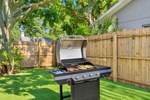 Un patio trasero con una parrilla, una cerca de madera y una casa al fondo.