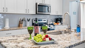Une cuisine avec des meubles blancs, un four à micro-ondes en acier inoxydable, un évier et un plan de travail en marbre.