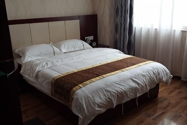 A neatly made bed with a headboard, a bedside table, and a window with curtains. - Kawaguchi Tenjiao Hotel (Hekou)