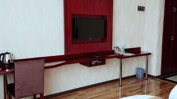 A room with a TV mounted on a red wall, a wooden desk with a chair, a bed, and a door.