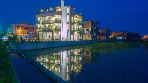 A modern multi-story building with balconies and reflective glass windows, situated next to a calm water body. - Colorful Fish Cottage (Yilan)