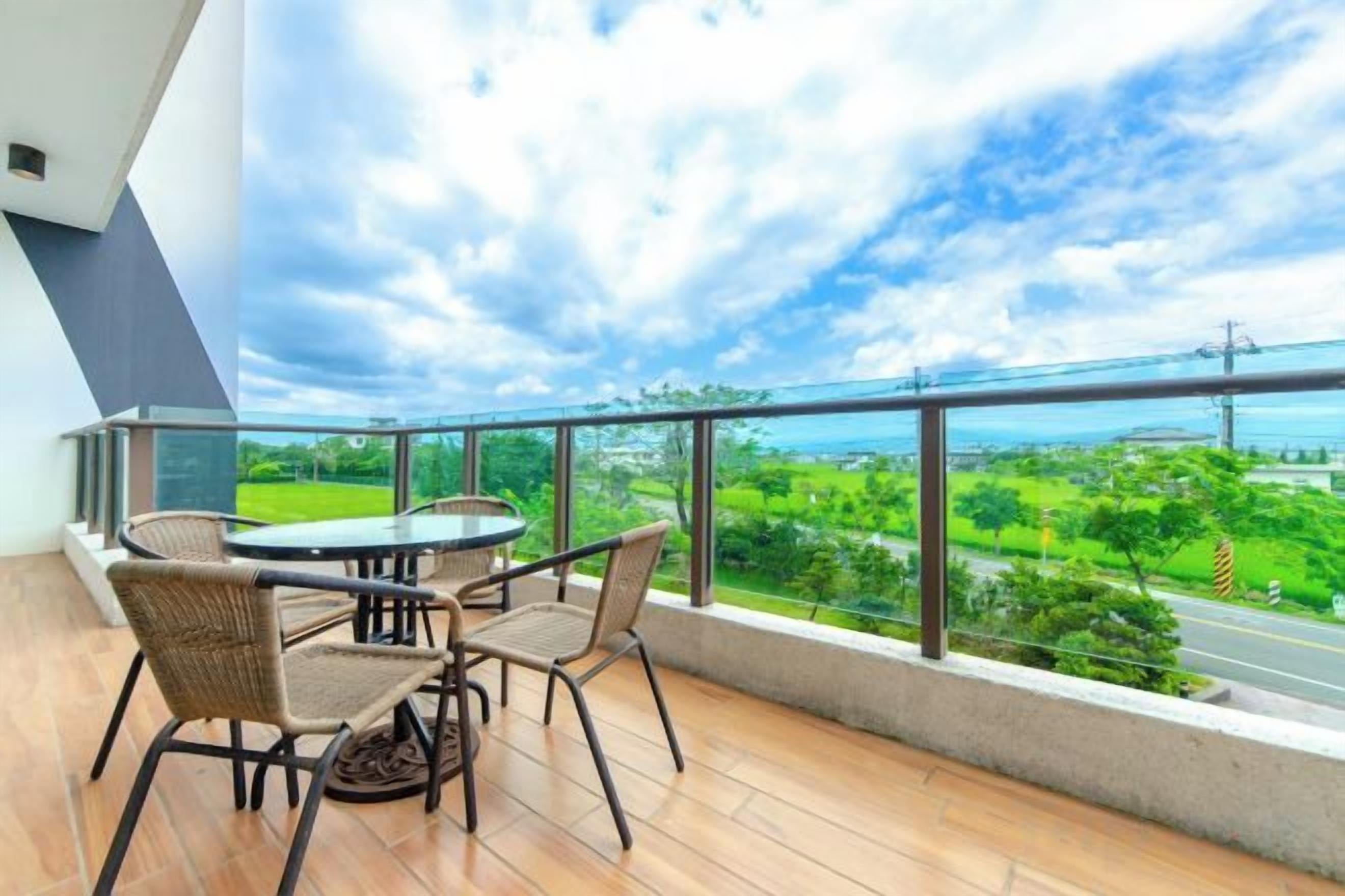 Un balcon avec une table et des chaises, donnant sur un paysage verdoyant et une route.