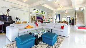 A spacious living room with a white sofa, blue ottomans, a glass coffee table, and a piano in the background. - Colorful Fish Cottage (Yilan)