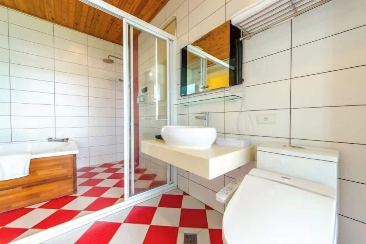 A modern bathroom with a checkered floor, a wooden bathtub, a glass shower enclosure, and a white toilet.