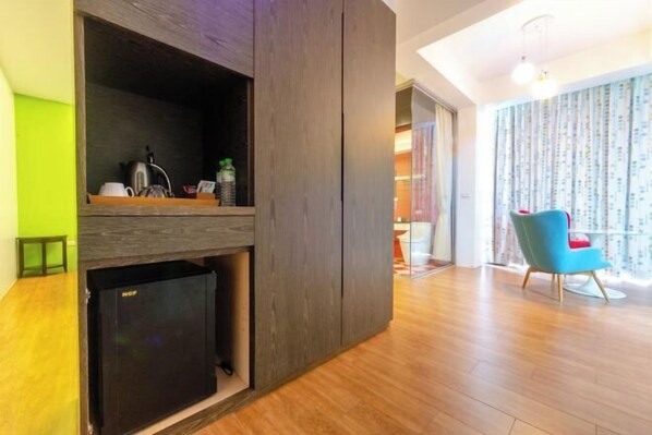 A modern living room with a built-in kitchen area, a blue chair, and a wooden floor.